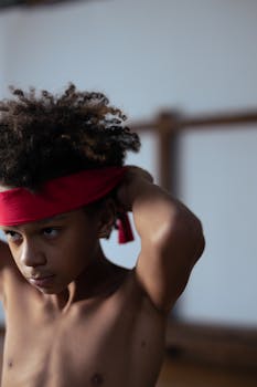 A focused young boy adjusting his red headband, preparing for martial arts practice.