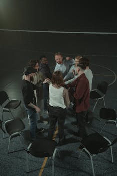 A group of adults engaged in a team-building activity indoors with chairs arranged in a circle.