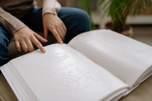 Child's hands explore a Braille book, encouraging tactile learning indoors.
